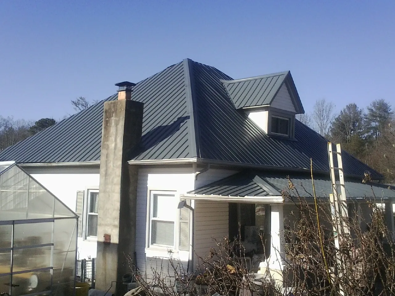 Dark blue standing seam metal roof on a white farmhouse with dormer — Slate & Tile Roof Repair by Roofing Brothers in Sauk City