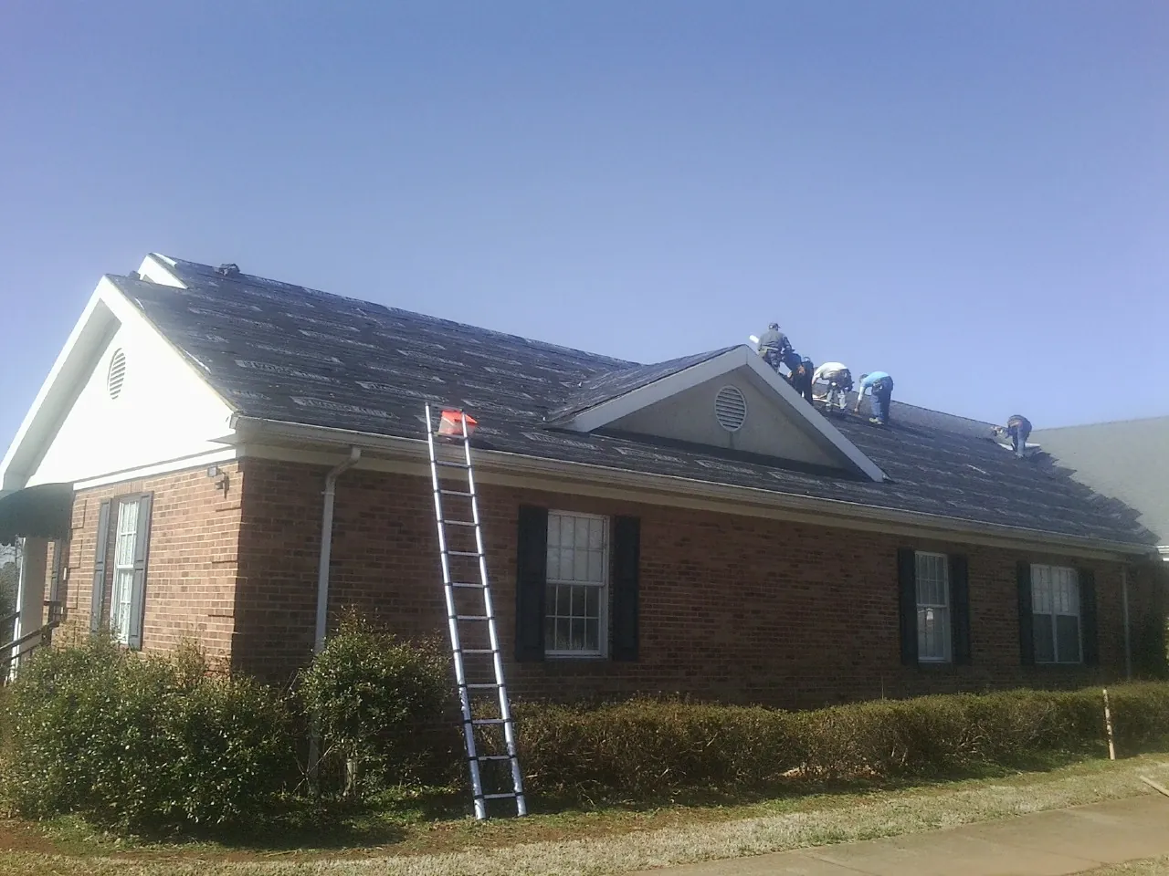 Crew tearing shingles off a brick ranch roof with a ladder set — Metal Roof Repair work by our crew in Sauk City