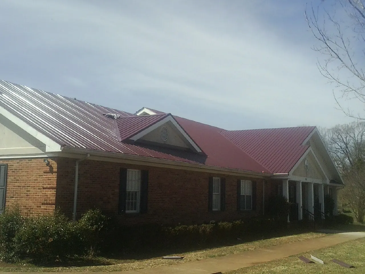 Red metal roof with gabled entries on a long brick building, from a Hail Damage Roof Repair job in Sauk City