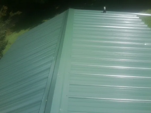 New green metal panels meeting at the ridge of a roof — Flat Roof Repair work by our crew in Sauk City