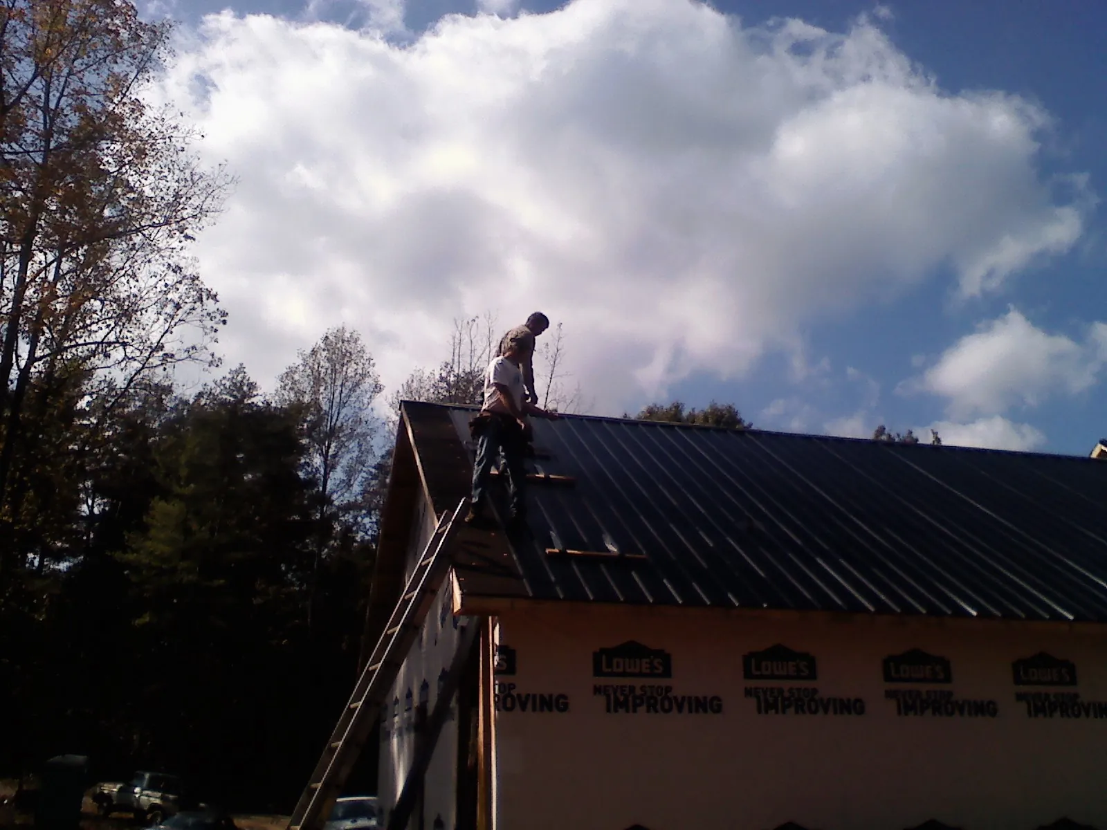 Roofer fastening dark metal panels high against a cloudy sky, from a Roof Inspection job in Sauk City
