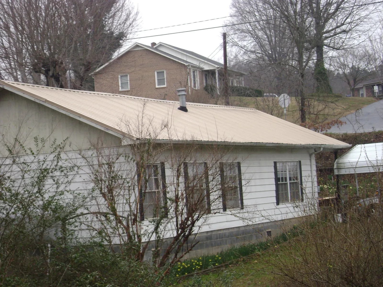 Tan metal roof on a white sided house set into a hillside — Commercial Roofing by Roofing Brothers in Sauk City