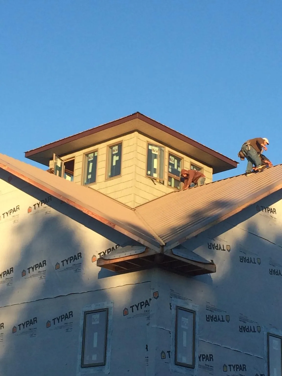 Roofers working around a rooftop cupola on a new metal roof at sunset — Roof Waterproofing in Sauk City by Roofing Brothers